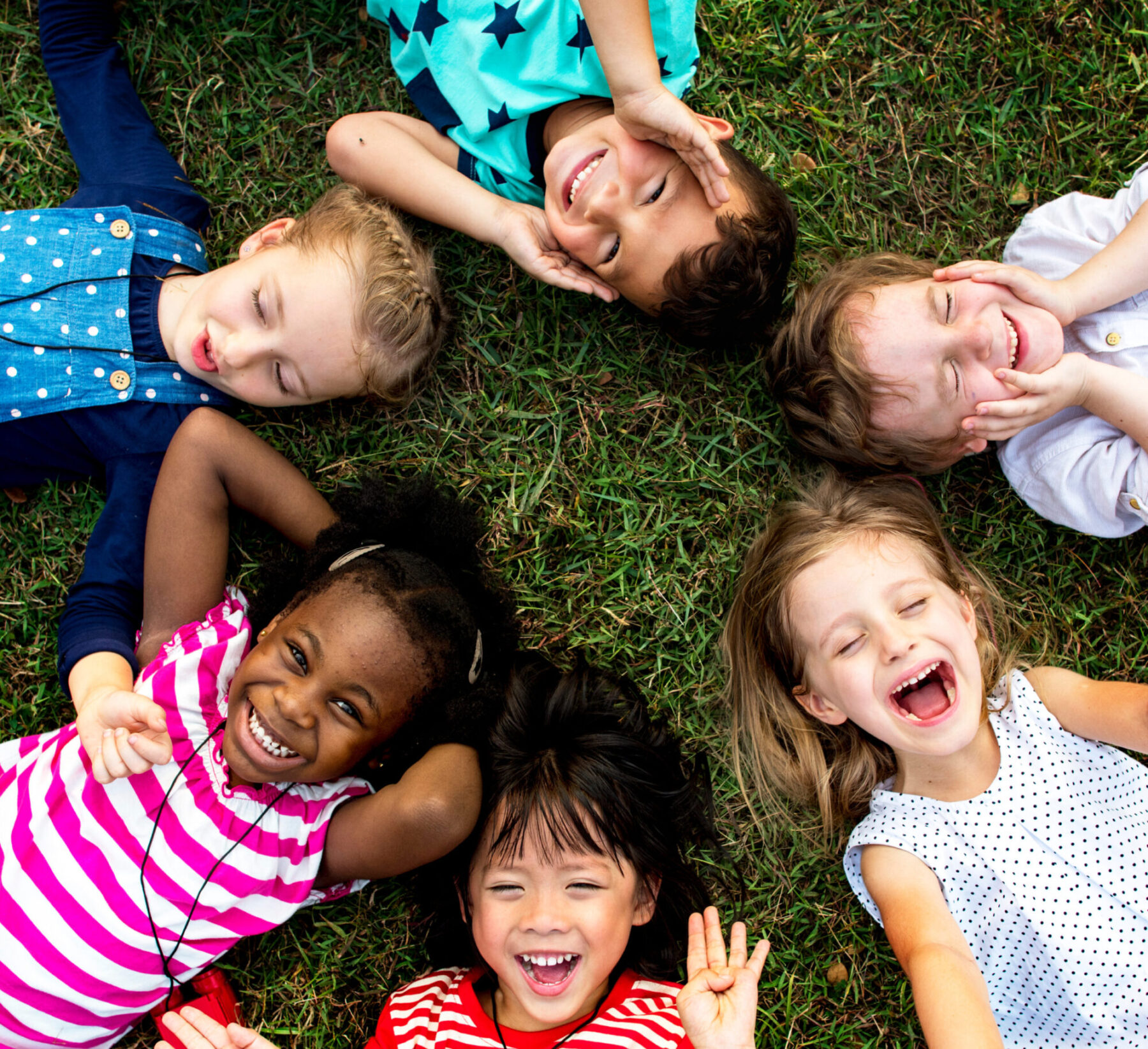 six diverse young children lay in the cross in a circle smiling at the camera